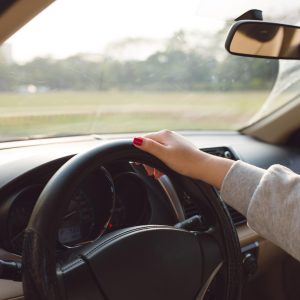 Close up of female hands on the steering. Traveler girl on car trip, looking at the road. View over shoulder