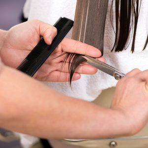 Close-up on female hairstylist hands cutting wet hair ends of brunette woman with scissors at beauty salon